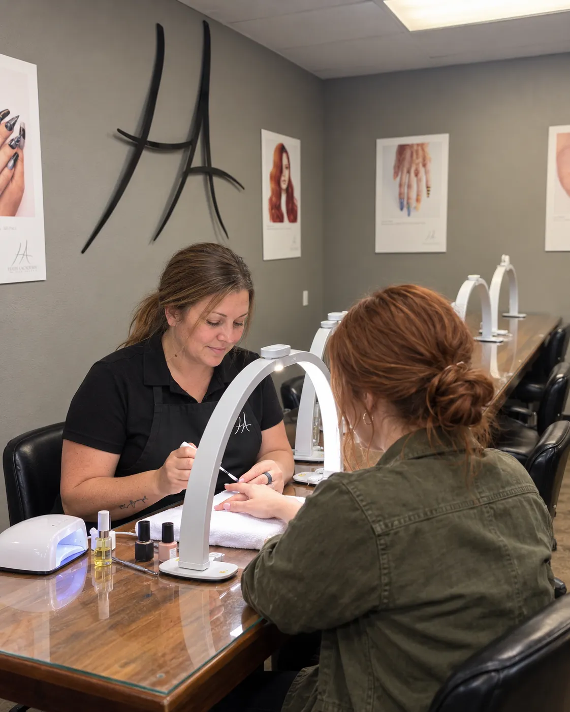 Nail technician in a Hays Academy apron painting a client's nails at the nail desk